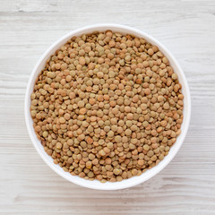 Organic green lentils in a white bowl on a white wooden surface, top view. Flat lay, overhead, from above. Close-up.