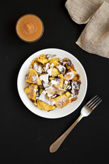 Homemade german Kaiserschmarrn pancake on a white plate on a black surface, top view. Flat lay, overhead, from above.