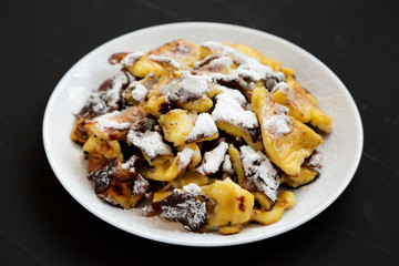 Homemade german Kaiserschmarrn pancake on a white plate on a black background, side view.
