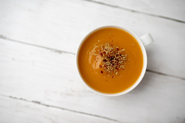 Creamy pumpkin squash vegetable soup in a white cup on white wood background