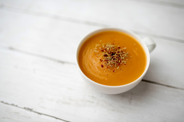 Creamy pumpkin squash vegetable soup in a white cup on white wood background