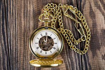 Vintage pocket watch on a chain lie on a wooden table. Roman numerals on the dial.