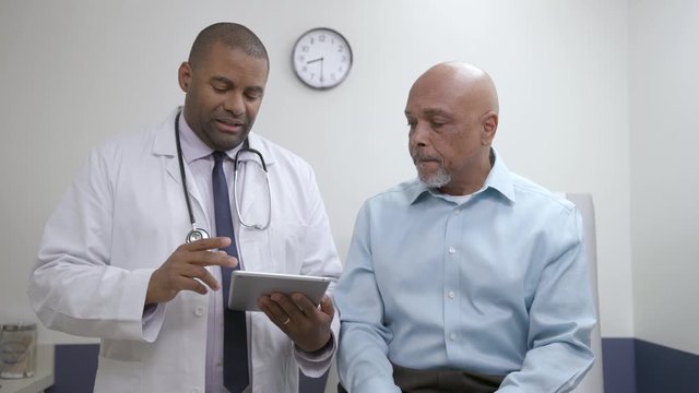 Doctor reviews chart with patient in doctor office, hospital exam room, serious