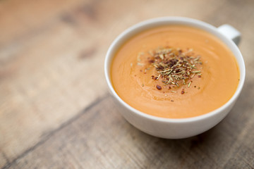 Creamy pumpkin squash vegetable soup in a white cup on wood background