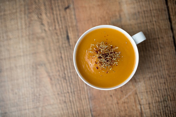 Creamy pumpkin squash vegetable soup in a white cup on wood background