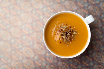 Creamy pumpkin squash vegetable soup in a white cup on tan background