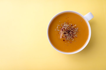 Creamy pumpkin squash vegetable soup in a white cup on yellow background