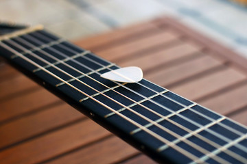 Guitar pick on the fingerboard of a brown guitar.
