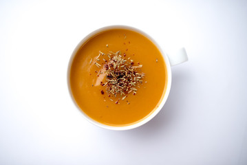 Creamy pumpkin squash vegetable soup in a white cup on white background