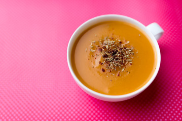 Creamy pumpkin squash vegetable soup in a white cup on pink background