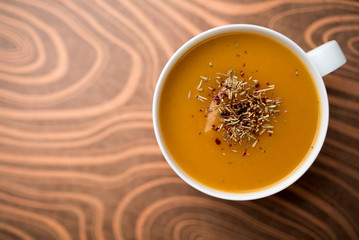 Creamy pumpkin squash vegetable soup in a white cup on tan background