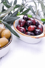 Traditional appetizers, green and red olives from Greek cuisine. White wood background. Fresh branches of olives. Copy space.