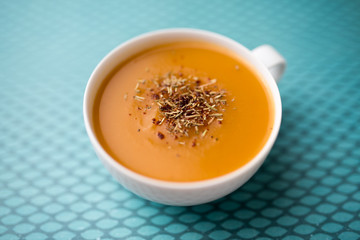 Creamy pumpkin squash vegetable soup in a white cup on blue background