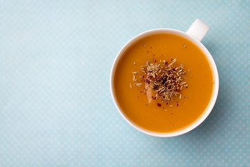 Creamy pumpkin squash vegetable soup in a white cup on blue background