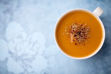 Creamy pumpkin squash vegetable soup in a white cup on blue background