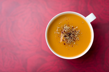 Creamy pumpkin squash vegetable soup in a white cup on red background