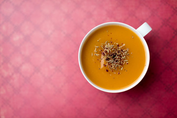 Creamy pumpkin squash vegetable soup in a white cup on red background