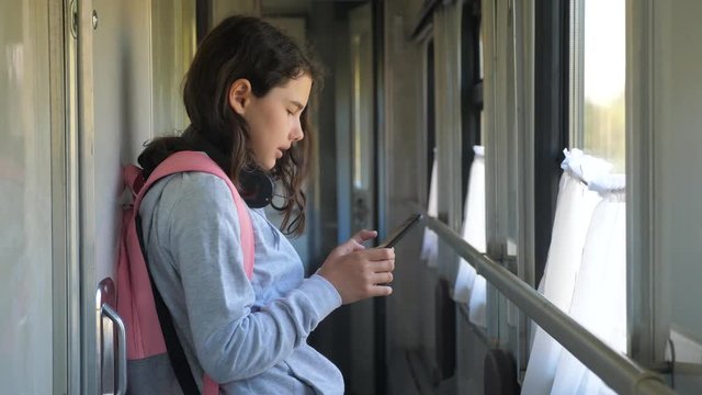 little girl walks on a train compartment car with a backpack and a smartphone. travel transportation railroad concept lifestyle . the girl in the train at the window corresponds the girl in the train