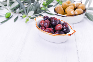 Traditional appetizers, green and red olives from Greek cuisine. White wood background. Fresh branches of olives. Copy space.