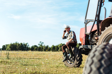 Plakat selective focus of agronomist talking on smartphone near tractor