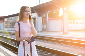 girl stands on the platform of the station with a suitcase and waits for a train, a student travels, leaves for summer vacation, copy space