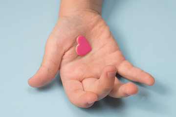 child's hand on a blue background with a pink heart in the palm