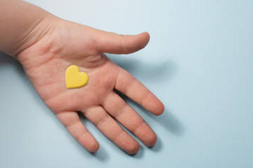 Fototapeta na wymiar child's hand on a blue background with a yellow heart in the palm