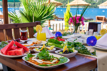 A healthy breakfast table composed of fried egg with cheese, orange juice, olives and watermelon served with flowers