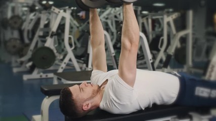 Muscular man in the gym lifts weights lying on a bench