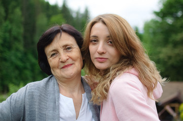 Fototapeta premium Close up portrait of happy smiling mother and daughter who are looking at the camera outside over landscape of forest and mountains.
