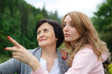 Happy senior woman with short dark hair and wrinkles on her face spending time together with her adult daughter, young girl is pointing at something. Concept of travelling with family