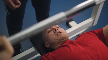 Guy raises the bar from his chest. Man raises free weight under control of instructor in sports club.