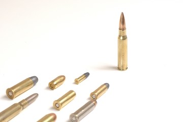 A large bullet (7.62 x 51mm NATO) standing in front of several smaller bullets laying over a white surface