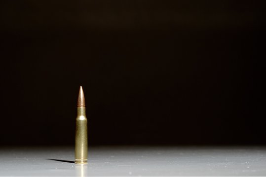 Large bullet (7.62 x 51 mm NATO) standing on a white surface with a black background