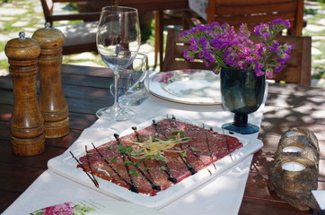 Top view of a thin sliced meat decorated by flowers and sauce on a wooden table