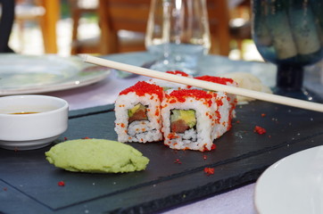 Close up view of a sushi served on a black plate with sauce and sticks