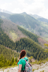 Naklejka na ściany i meble woman traveler with backpack looking at amazing mountains and forest, wanderlust travel concept, space for text, atmospheric epic moment
