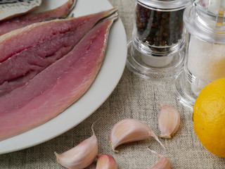 Fresh mackerel fillets on a white plate, Garlic cloves, lemon, salt and pepper shaker in the background. Sea food preparation stage.