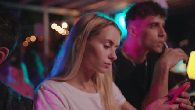 Row of attractive friends sitting by bar counter chilling with alcohol drinks communicating staying at the party. Communication and people concept.