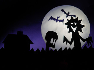 Dark Halloween season background with moon in the background and scary creatures silhouettes. Alien scull, bats, and funny monster. Copy space.