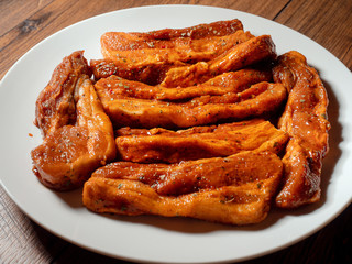 Fresh uncooked pork belly slices in barbecue marinate on a white plate.