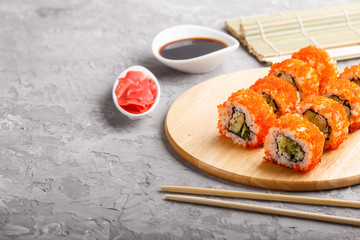 Japanese maki sushi rolls with flying fish roe on wooden board on a gray concrete background. Side view, copy space.