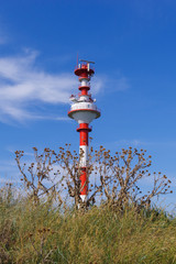 Modern navigation lighthouse on the Baltic Spit. The lighthouse is painted in red and white stripes. In the foreground is dry, prickly grass. The creation of nature and the creation of man are nearby.