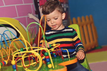 A little boy in a colored striped raglan plays a toy for fine motor skills.