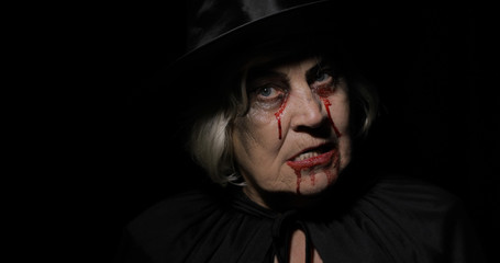 Old witch Halloween makeup. Elderly woman portrait with blood on her face.