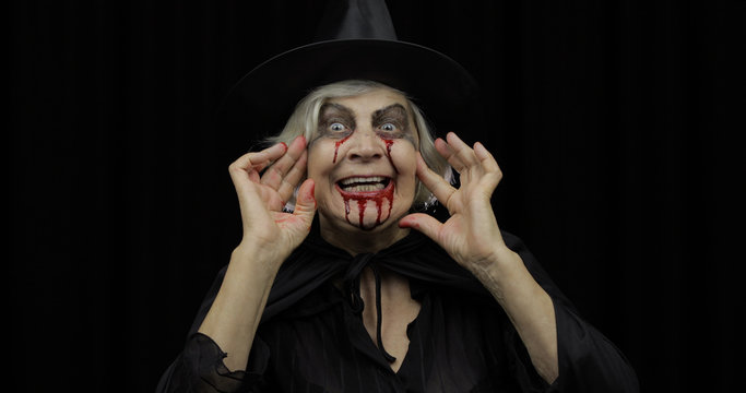 Old witch Halloween makeup. Elderly woman portrait with blood on her face.