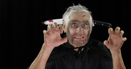 Elderly man with knife in head. Halloween makeup and costume. Blood on his face
