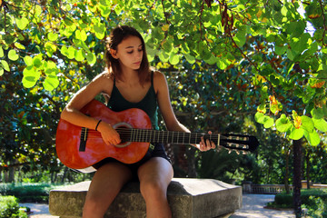 Music Concept: Young and Beautiful woman playing Spanish guitar outdoors in a park.