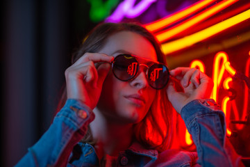 Portrait of a young girl in sunglasses in the night city, with creative light on the background of...