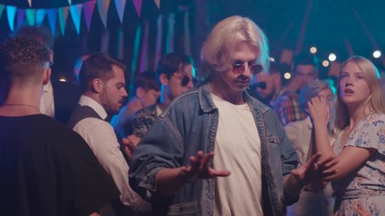 Attractive blonde guy rocking the party off dancing like boss among his fashionable friends at socializing gathering event.